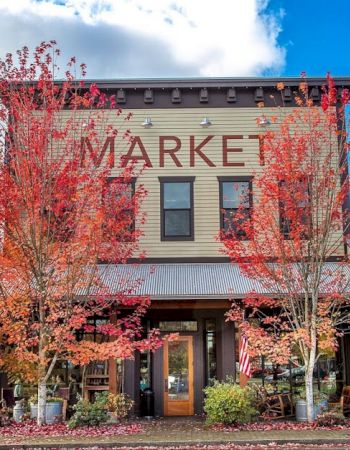 A two-story building labeled "MARKET" is surrounded by autumn trees with red leaves, under a blue sky with clouds.