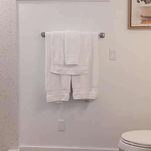 A bathroom with white towels on a rack, a toilet, a vanity, and a picture of a dog in a bathtub on the wall.