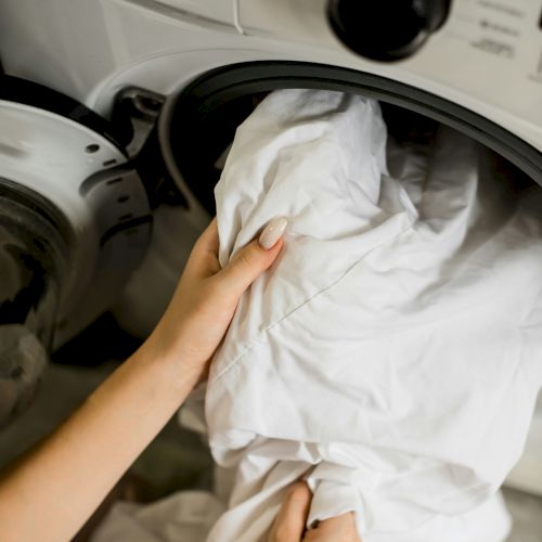 A person is loading or unloading white laundry from a front-loading washing machine, visible in a home environment.